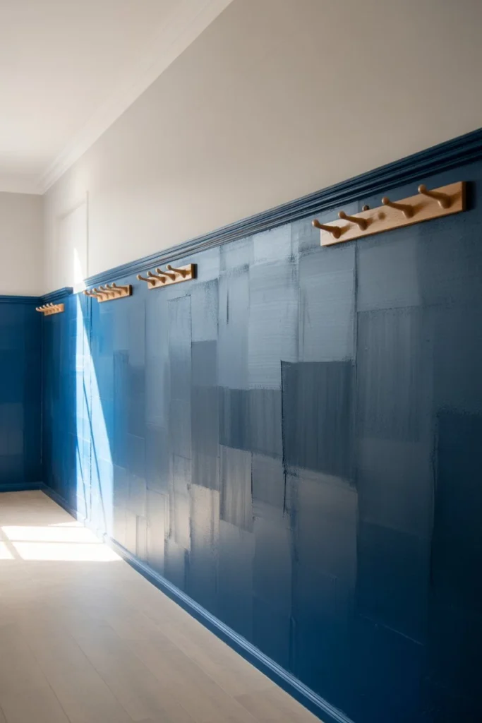 A 20mm wide-angle, eye-level shot of a hallway featuring a two-tone color block wall. The bottom third is painted a matte deep navy, and the top is a crisp off-white. The camera captures the full length of the hallway, showing a few simple hooks for coats. Natural light from a side window shows the realistic texture of the paint and the sharp, hand-taped horizontal line. 8k resolution, Pinterest-friendly aesthetic.