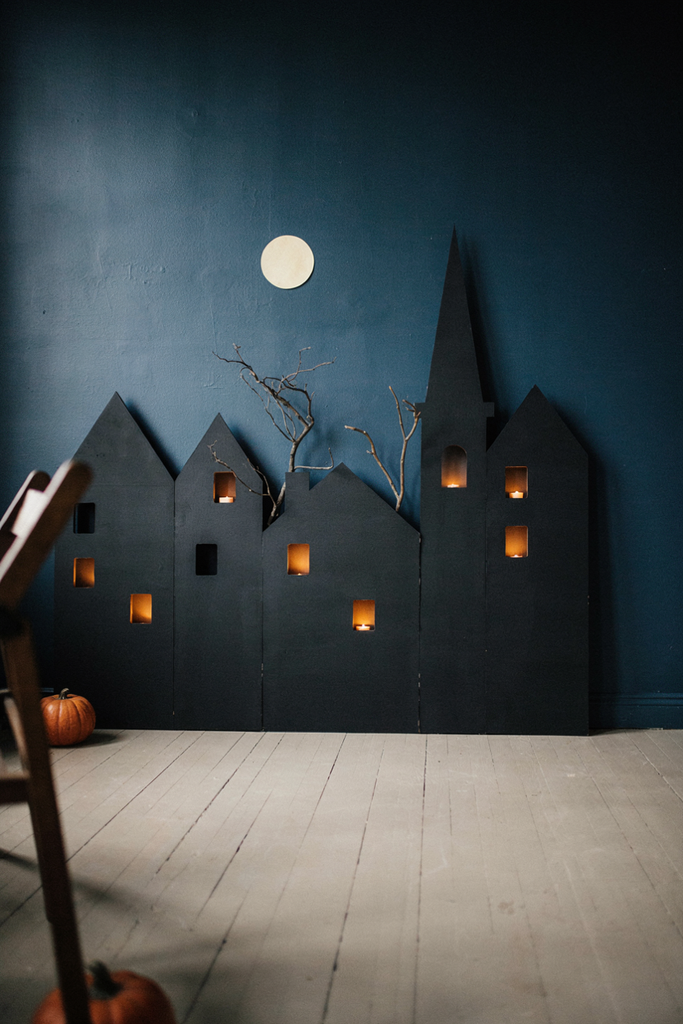 Black foam board haunted house skyline with glowing windows on a navy wall under a paper moon