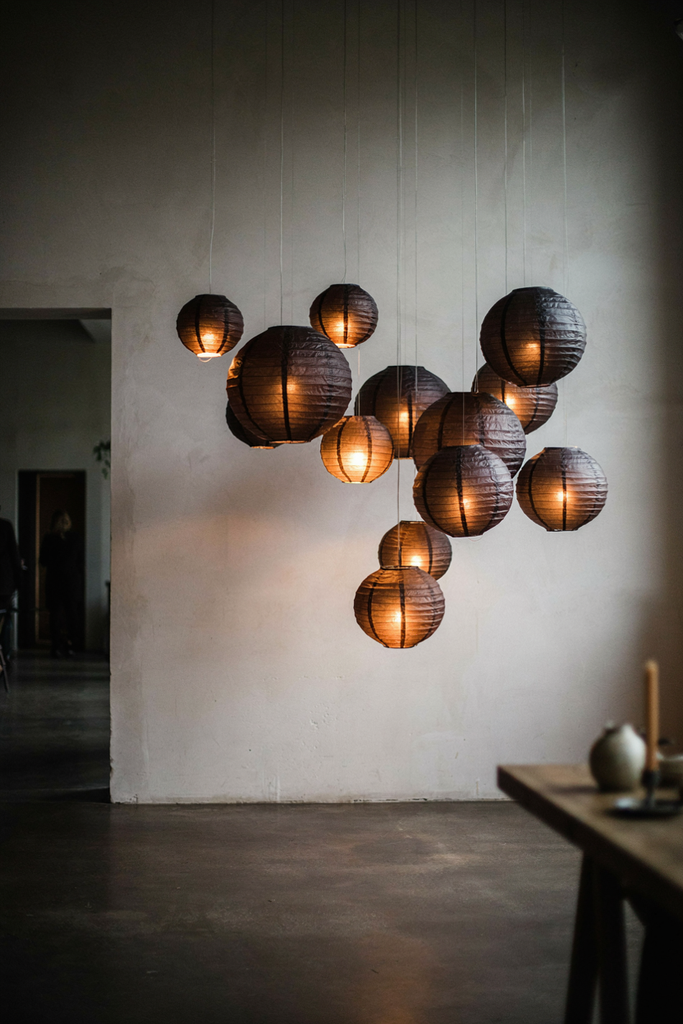 Fourteen black paper lanterns glowing amber at different heights in front of a bone wall