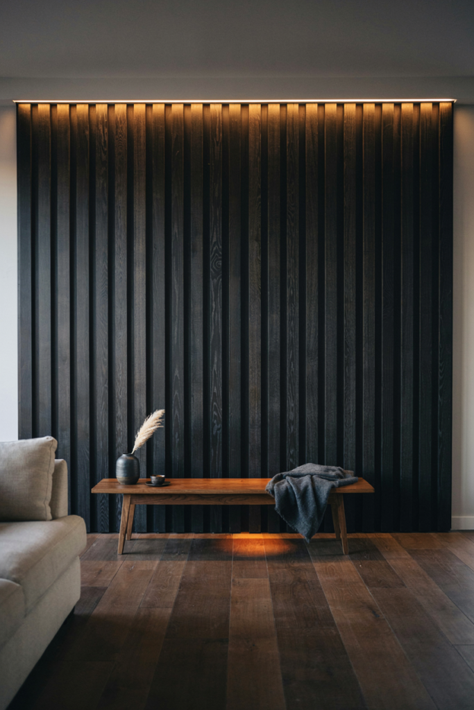 Black-stained oak slat panel lit from above with ribbed shadows behind a low bench