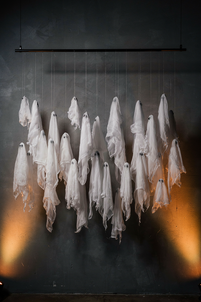 Strands of white cheesecloth ghosts hanging at varied heights against a charcoal wall