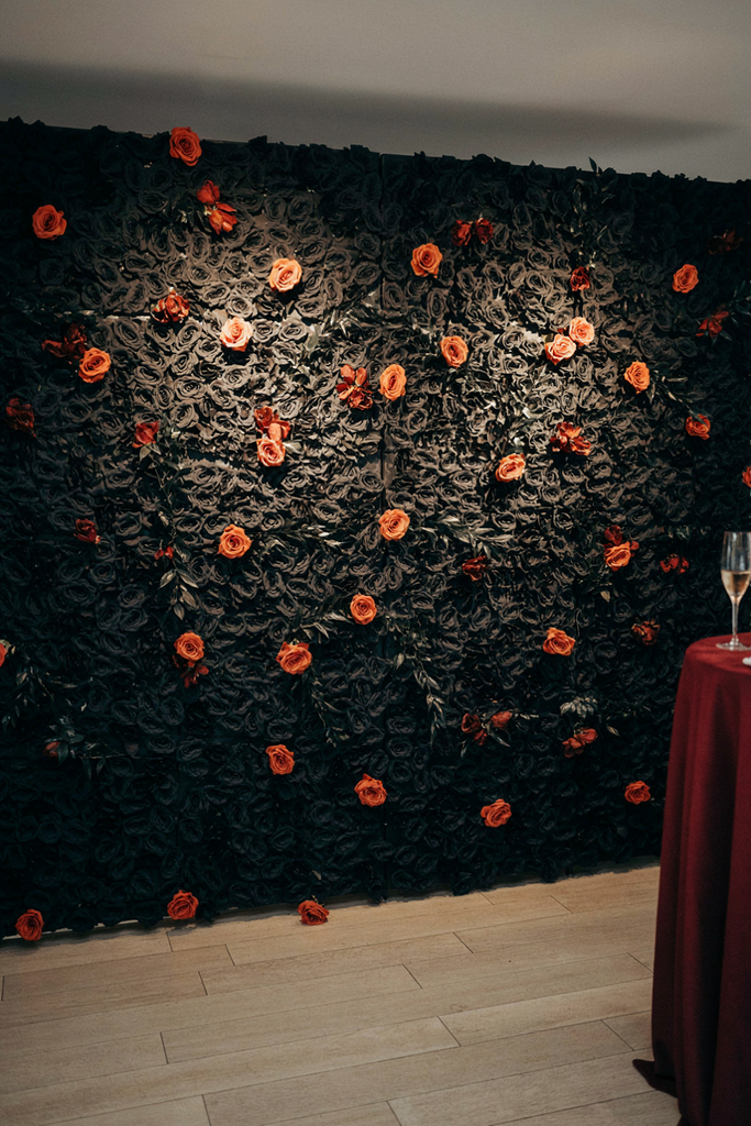 Wall of black faux roses with orange accents lit by two warm ceiling spotlights