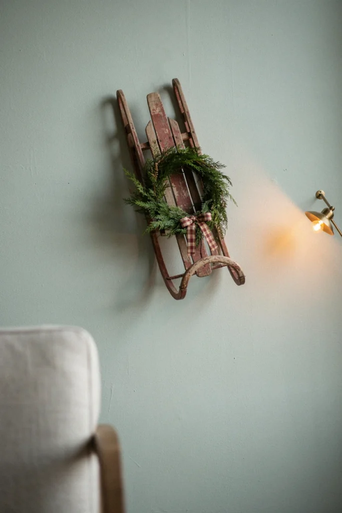 Vintage wooden sled hung at an angle with a wreath and plaid bow on a sage wall