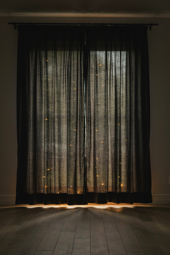 Layered black sheer curtains with warm fairy lights glowing behind them on a party wall