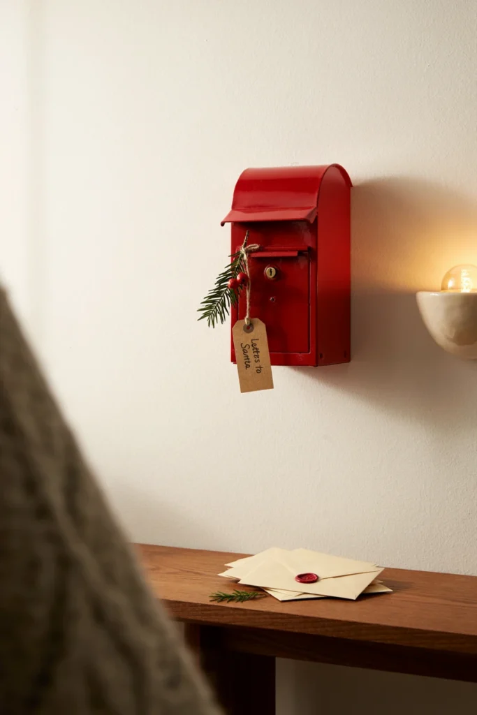 Small red wall mailbox with a cedar sprig and a Letters to Santa tag on a white wall