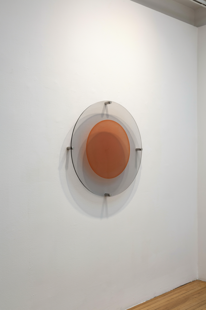 Smoked acrylic disc on standoffs with an orange circle showing through on a bone wall
