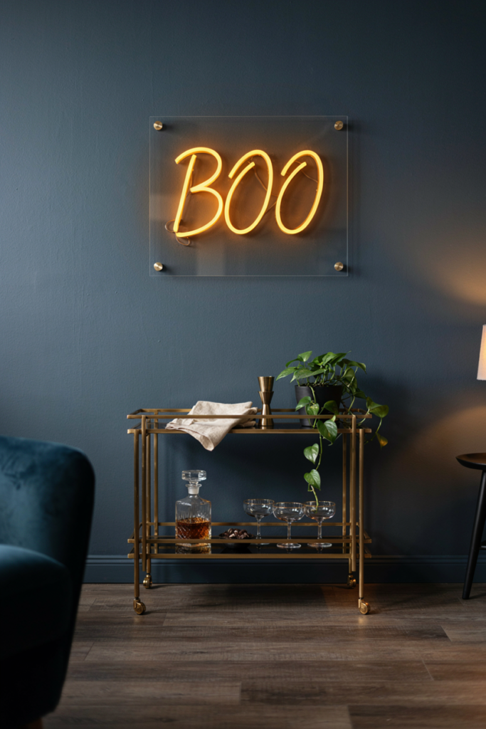 Amber neon sign spelling Boo glowing on a charcoal wall above a brass bar cart