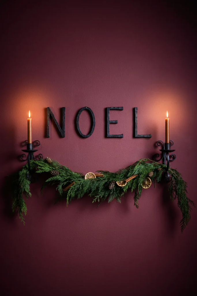 Black iron letters spelling Noel on a cranberry wall with a cedar swag and candle sconces