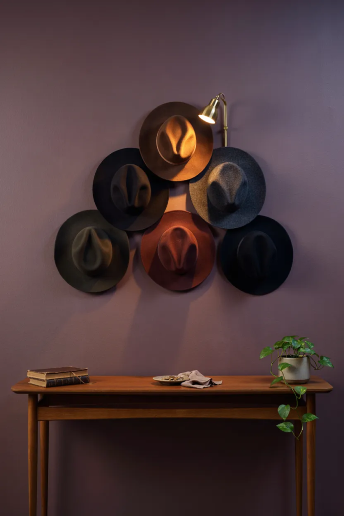 Five wool-felt witch hats hung in a staggered cluster on an aubergine entryway wall above a console